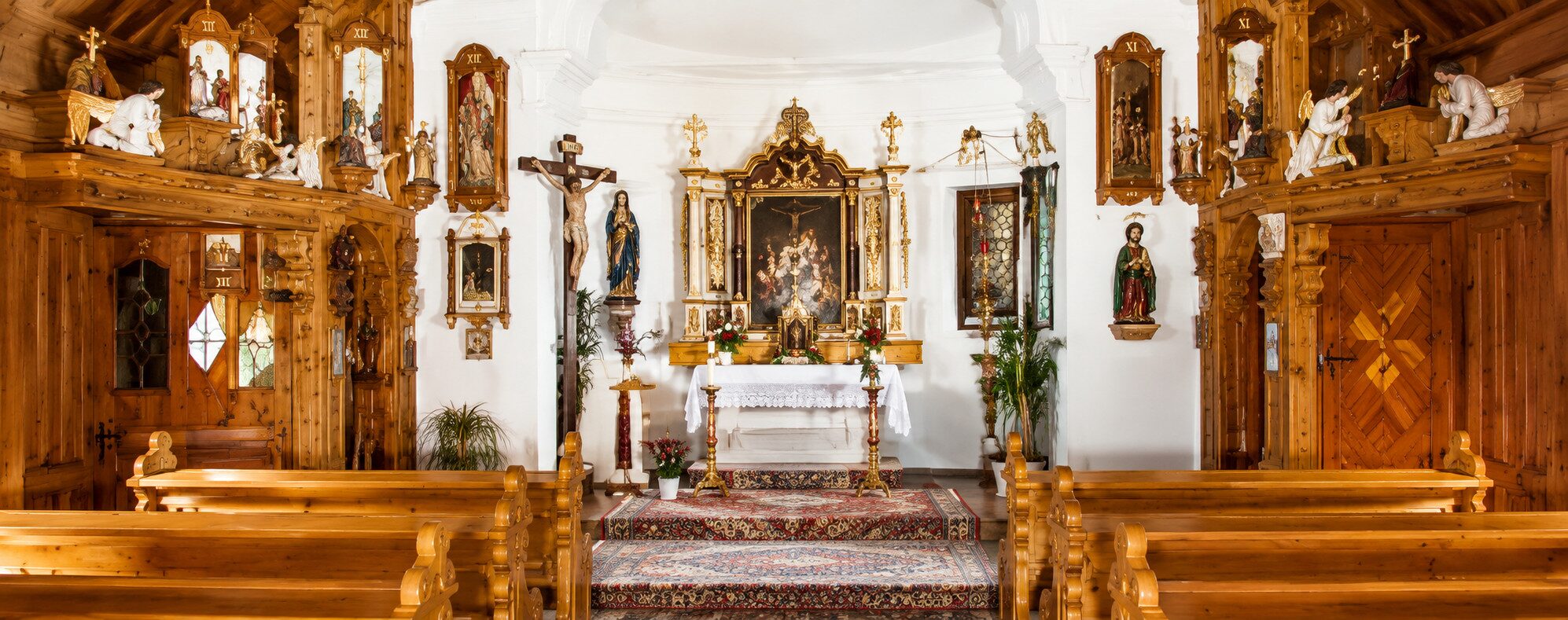 Blick in den Altarraum der neuen Tussetkapelle: geschnitzter Altar mit dem Gnadenbild, Kruzifix, Kreuzwegbilder und Holzbänke
